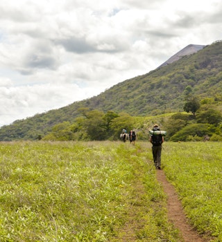 San Jacinto, Nicaragua - June 18, 2015: Group of hikers walks through the field and is about to ascend the slopes of the very active Telica volcano in San Jacinto, Leon, Nicaragua. Central America