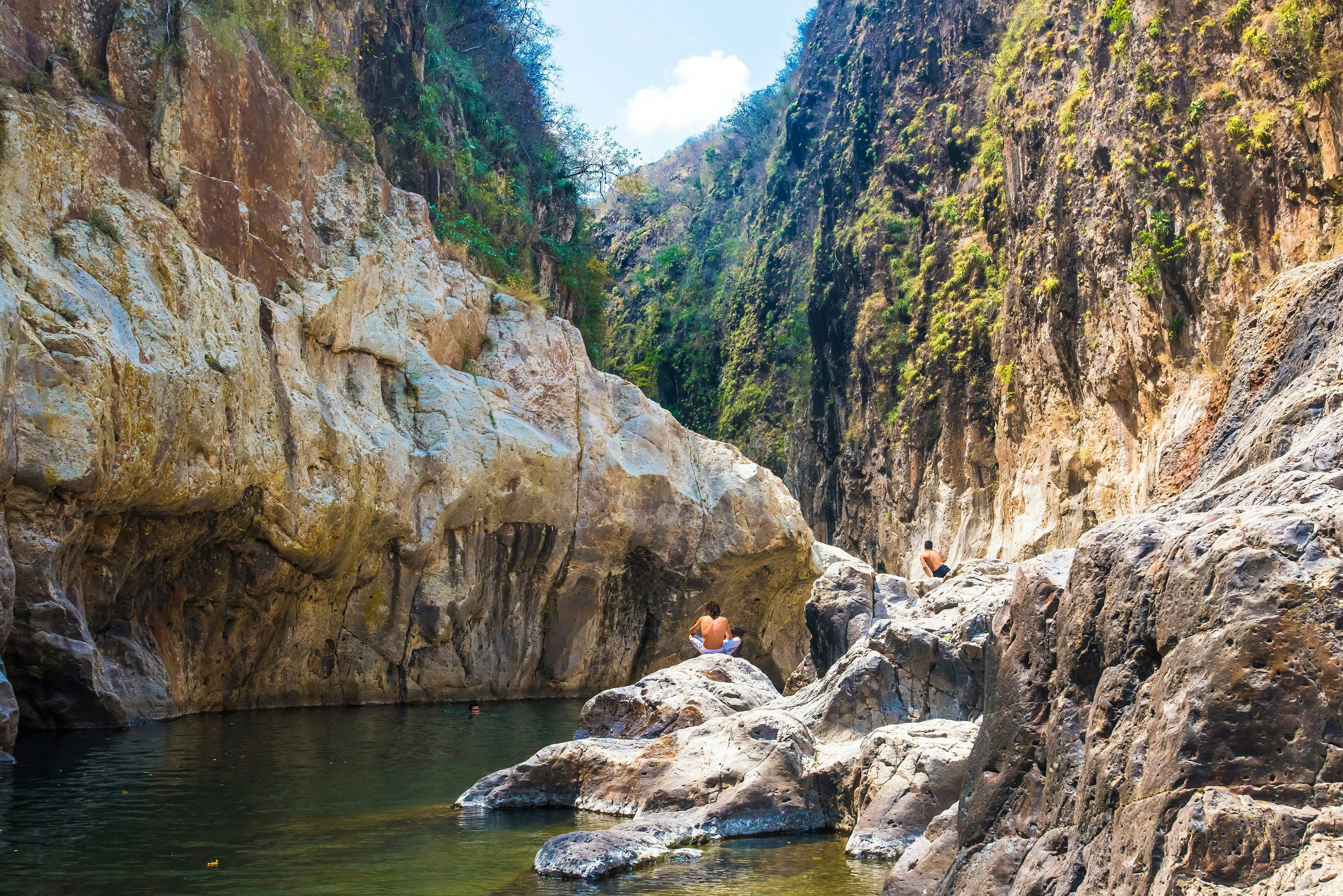 Somoto Canyon, Nicaragua. Man in the distance sitting in a stone contemplating the peaceful stream of water flowing through the rock mountains. Beautiful dry summer natural scenery.; 
Monumento Nacional Cañon de Somoto

Shutterstock ID 1822814987; your: Bridget Brown; gl: 65050; netsuite: Online Editorial; full: POI Image Update
