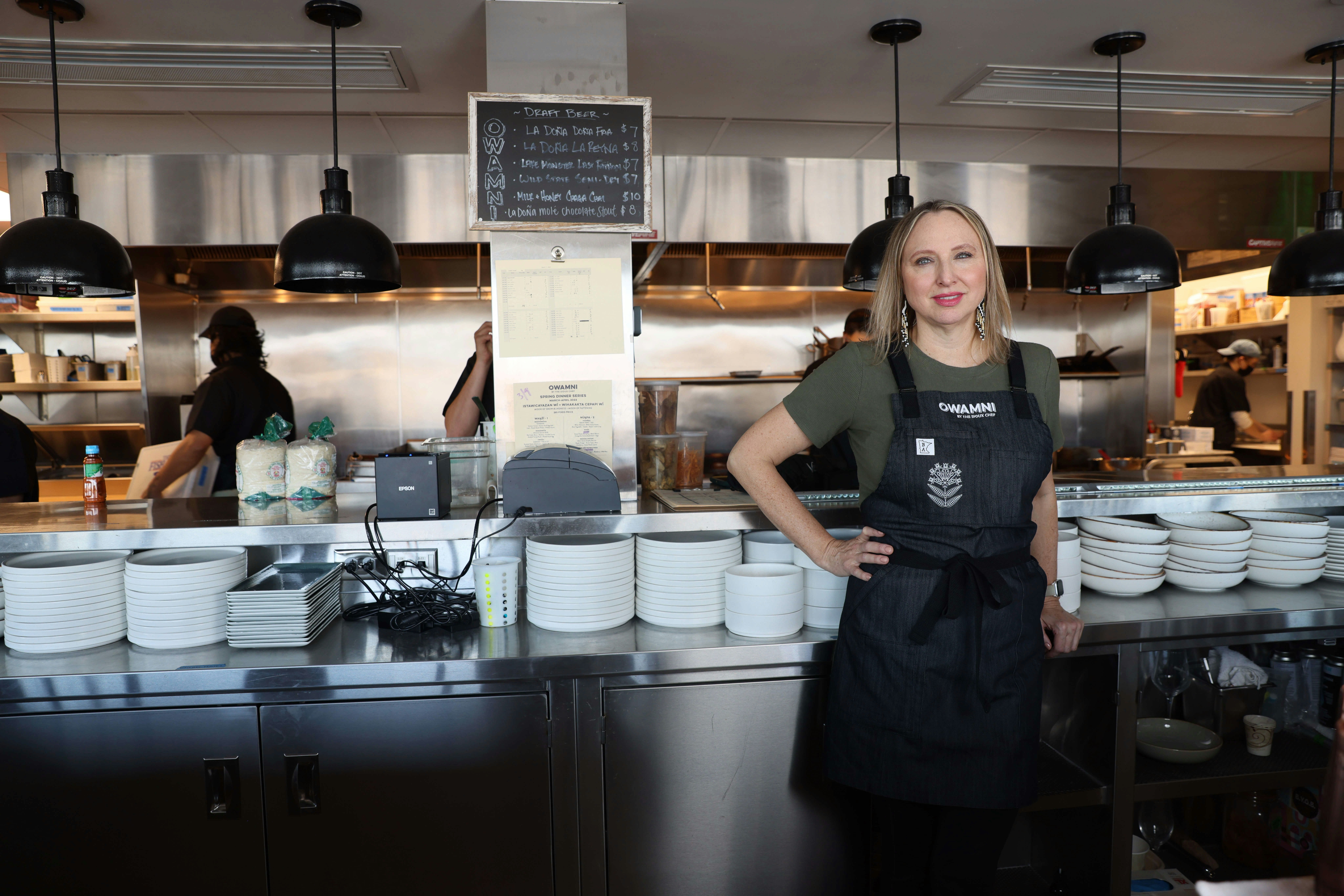 Dana Thompson stands in the Owamni by The Sioux Chef kitchen with staff 