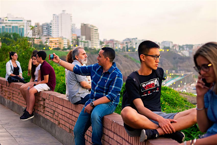 Peruvian people and tourists in Lima, watching the sunset and taking selfies at Malecón de la Costa Verde