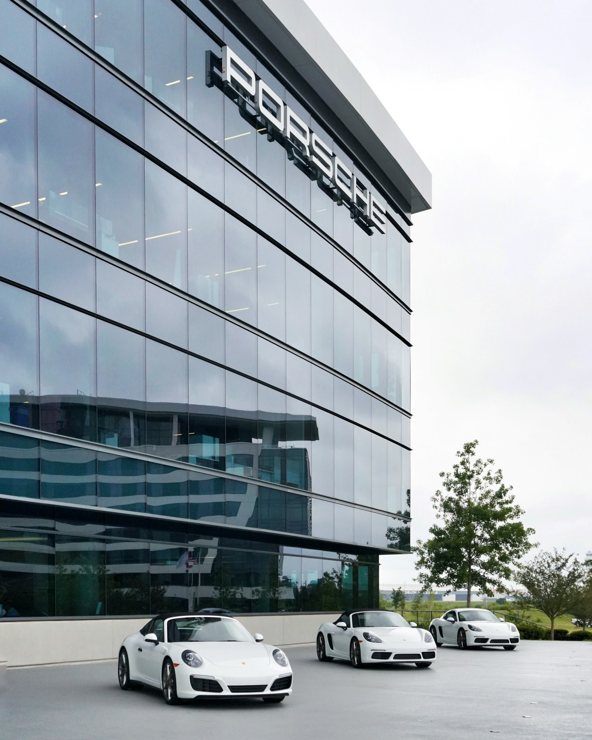 A trio of white Porsches are lined outside the glass building of the Porsche Experience Center in Atlanta. 