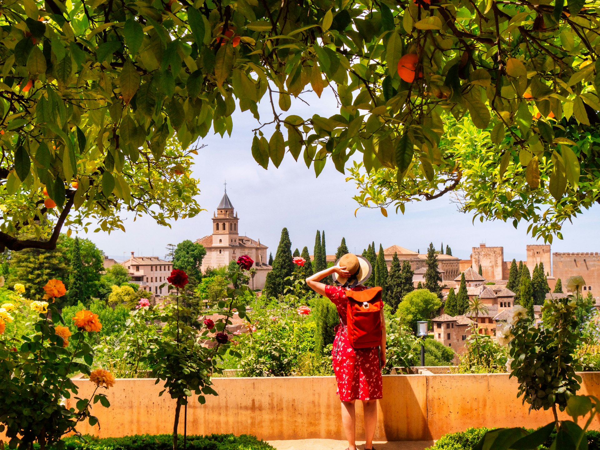 A woman stands beneath orange trees looking at the Alhambra in Granada