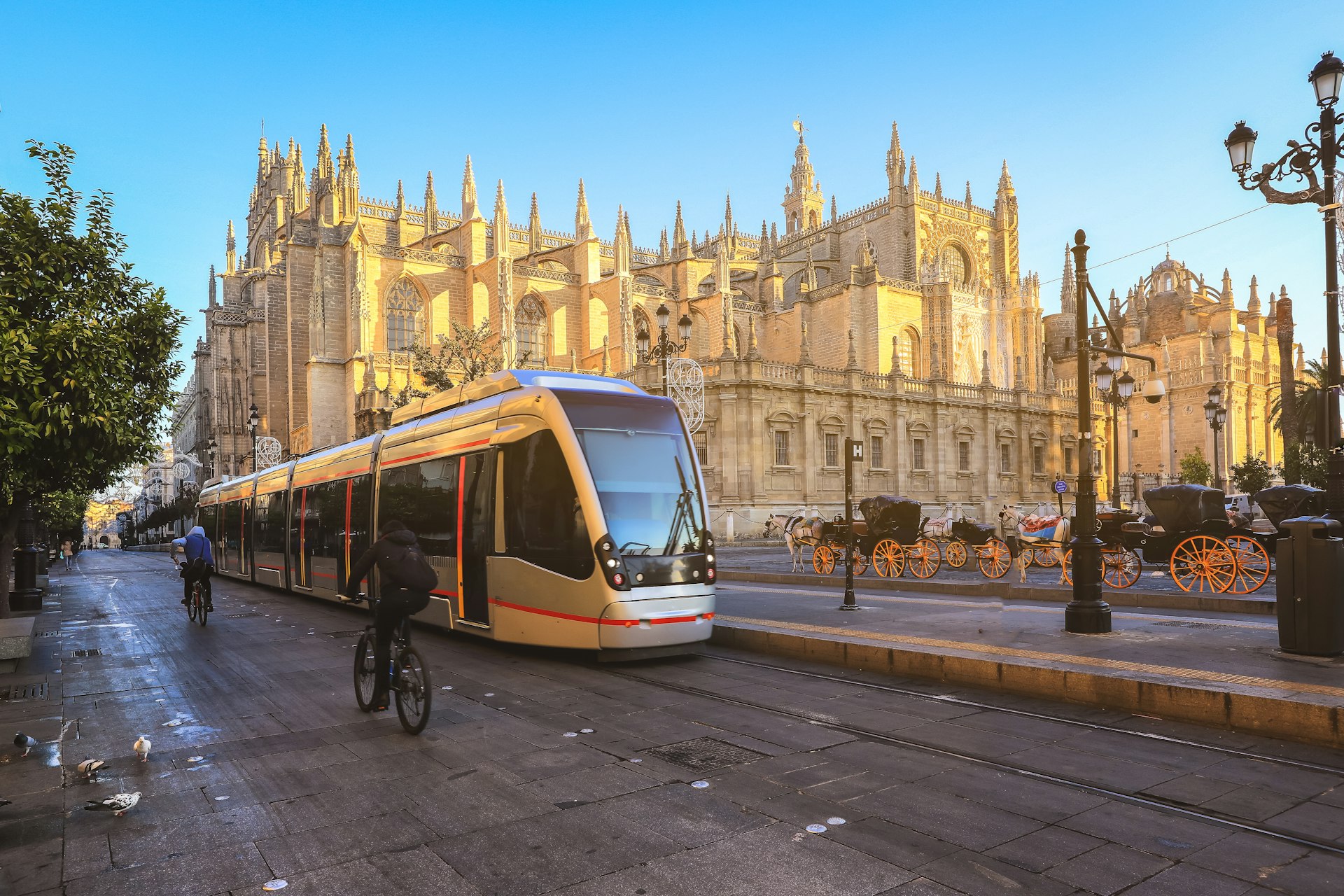 A tram passes in front of a huge Gothic cathedral building on a sunny day