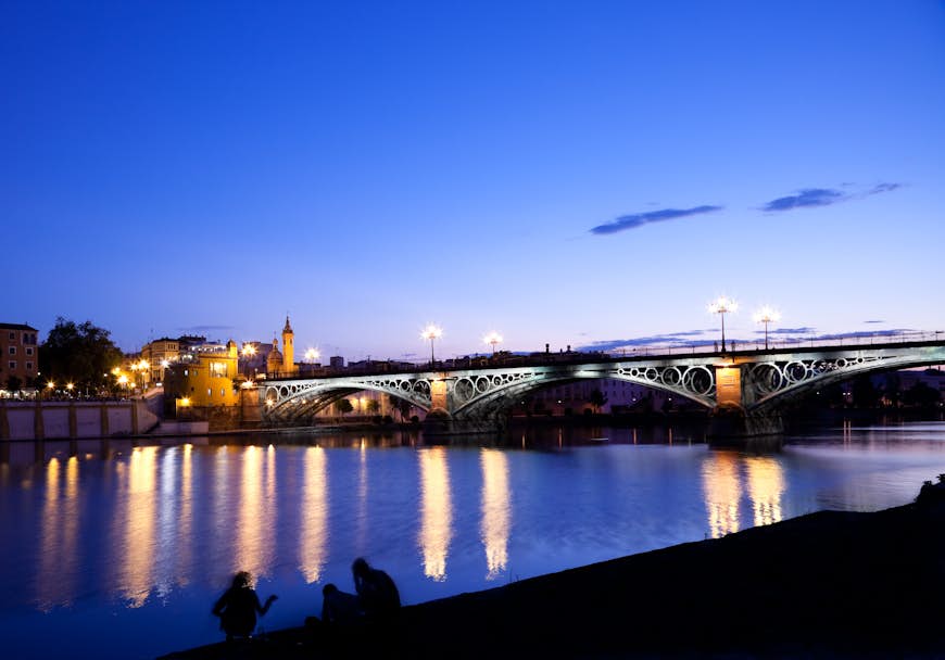 Trianabron som spänner över floden Guadalquivir i Sevilla upplyst på natten