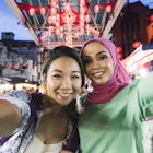 Two friends, one chinese young woman and one muslim mid adult woman,  having a selfie at the market together