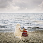 Toddler boy sitting with golden retriever dog on beach looking at lake