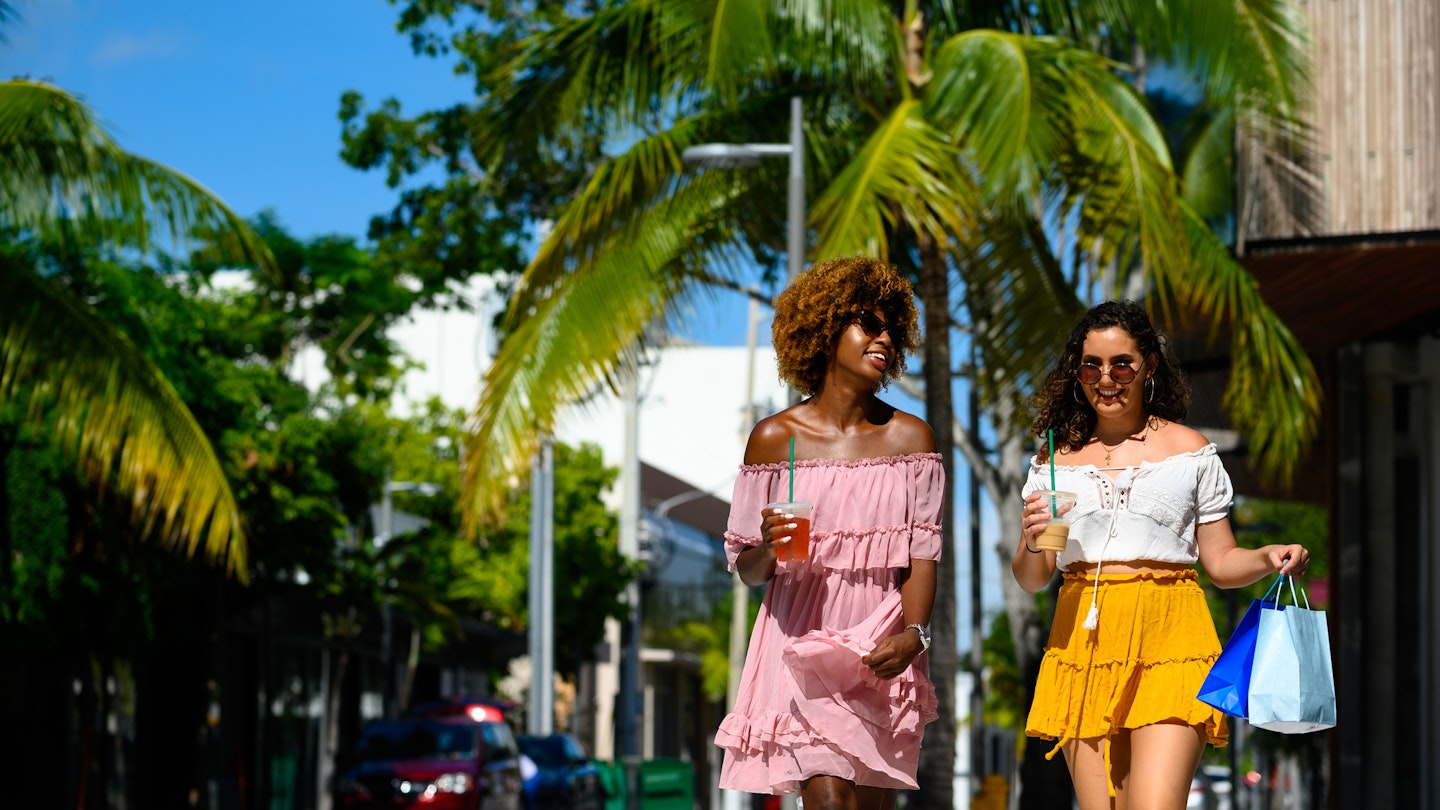 Female friends holding shopping bags and drinks in city. Young women are walking on street during summer. They are enjoying city life on sunny day