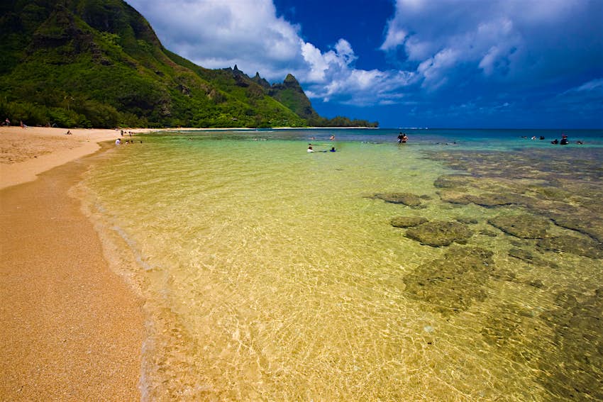 You can access Makua beach from Haʻena State Park People in the water at Tunnels beach in Kauai, with a view of Makana peak (aka Bali Hai) in the distance