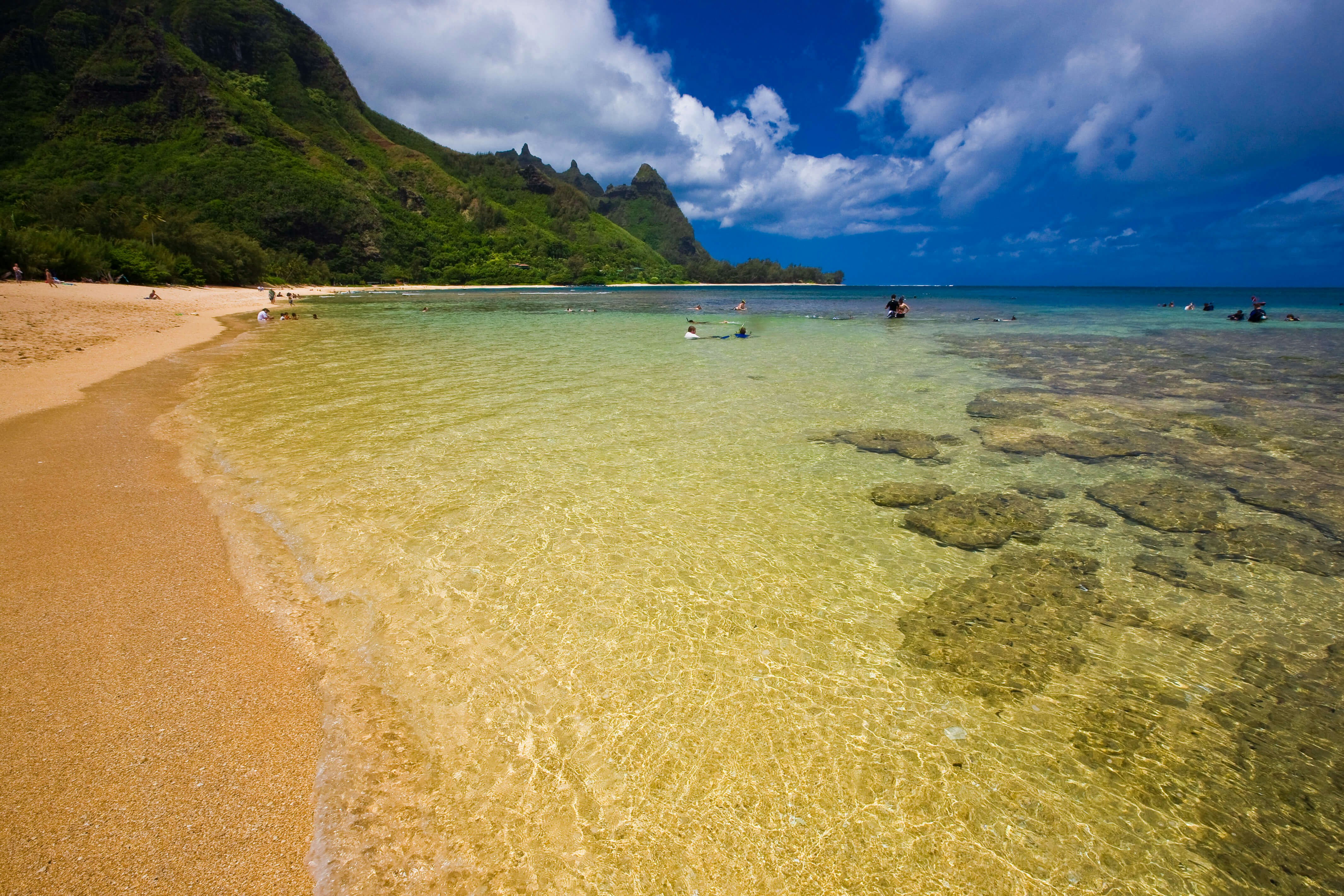 People in the water at Tunnels beach in Kauai, with a view of Makana peak (aka Bali Hai) in the distance