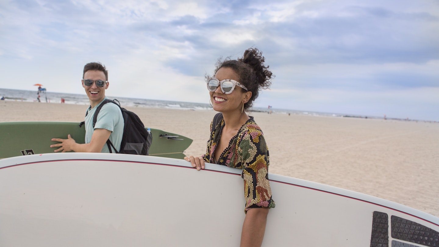 Young couple carrying surfboards on Rockaway Beach, New York State, USA