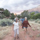 A multiethnic group of friends walk through the Utah desert. Two females are in front - one in her 20s, one in her early 60s.