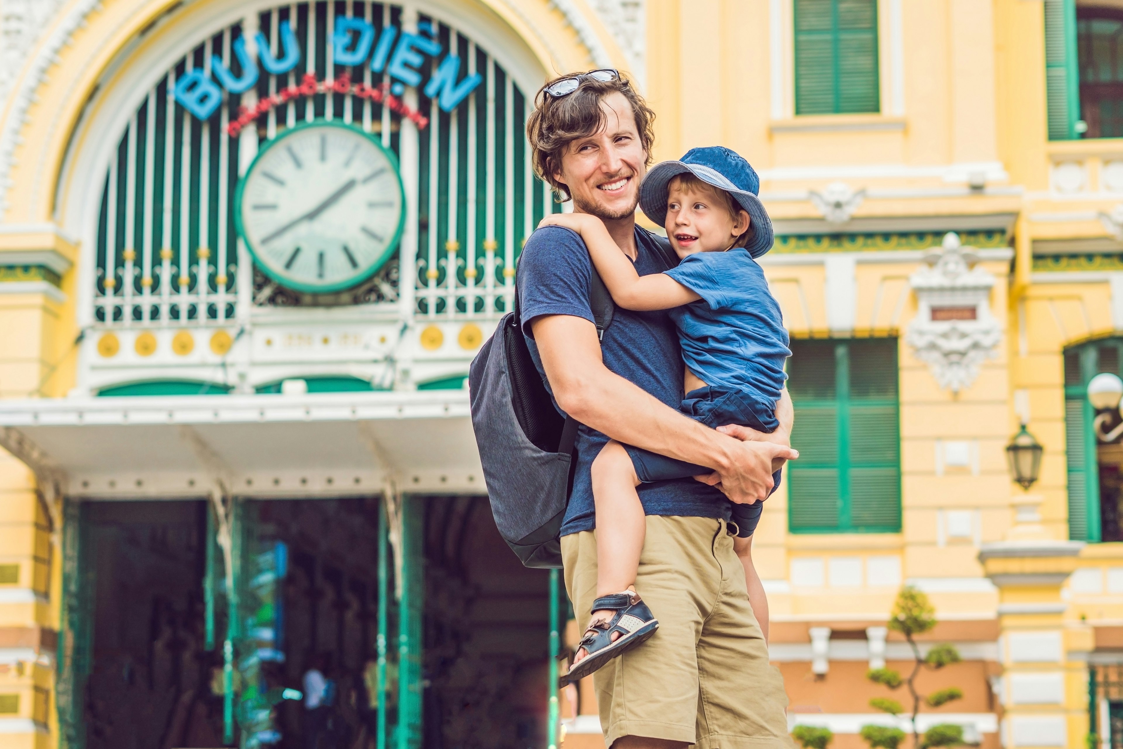 Father and son on background Saigon Central Post Office on blue sky background in Ho Chi Minh, Vietnam. The inscription on the Vietnamese "post office"; Shutterstock ID 1036242475; your: Claire Naylor; gl: 65050; netsuite: Online ed; full: HCMC free update