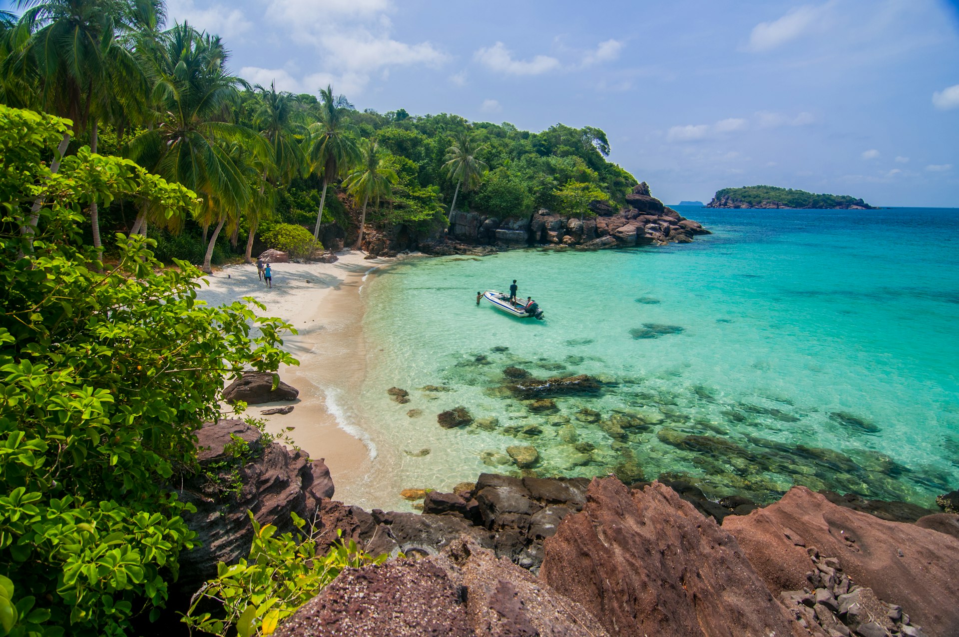 A sandy cove with turquoise ocean backed by lush jungle. A single motorboat is in the bay