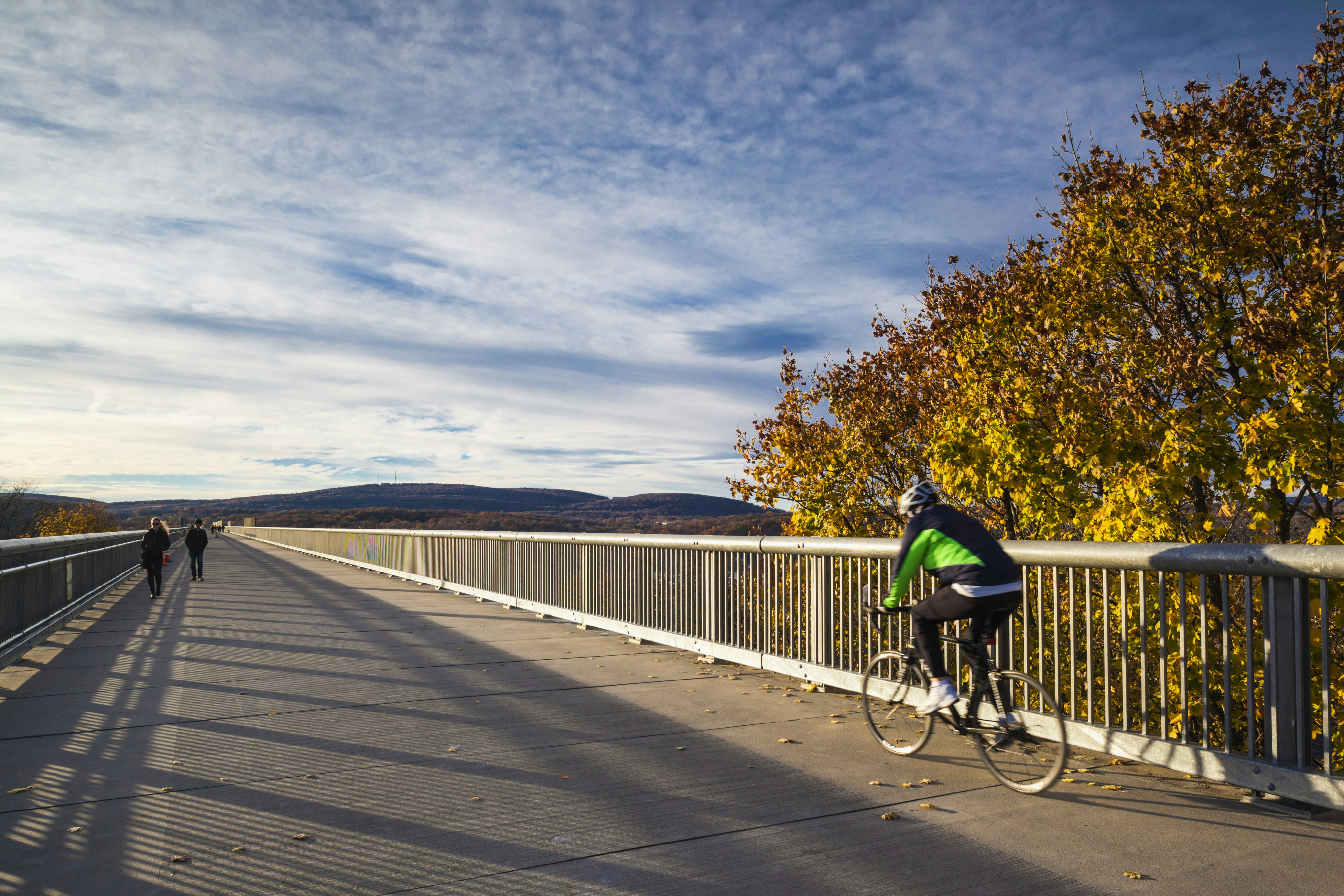 A cyclist bikes across the Walkway Over the Hudson in Hudson NY. There's a couple walking in the opposite direction. 