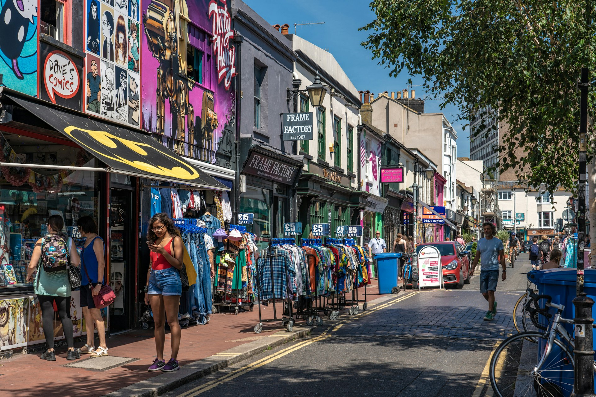 Shoppers wander along a street with brightly colored shop fronts and rails of clothes