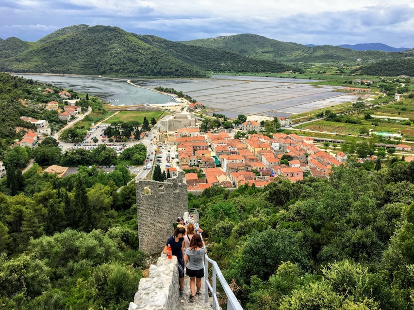 Ston, Croatia - July 9th, 2019: A group of tourists walking down along the the Walls of Ston, towards the ancient town of Ston, Croatia below.
