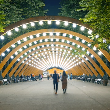The main wooden arch with light and walking people in Sokolniki park, Moscow,  Russia
