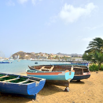 A collection of fishing boats beached on Mabota Beach in Mindelo with more luxurious sailboats in the background