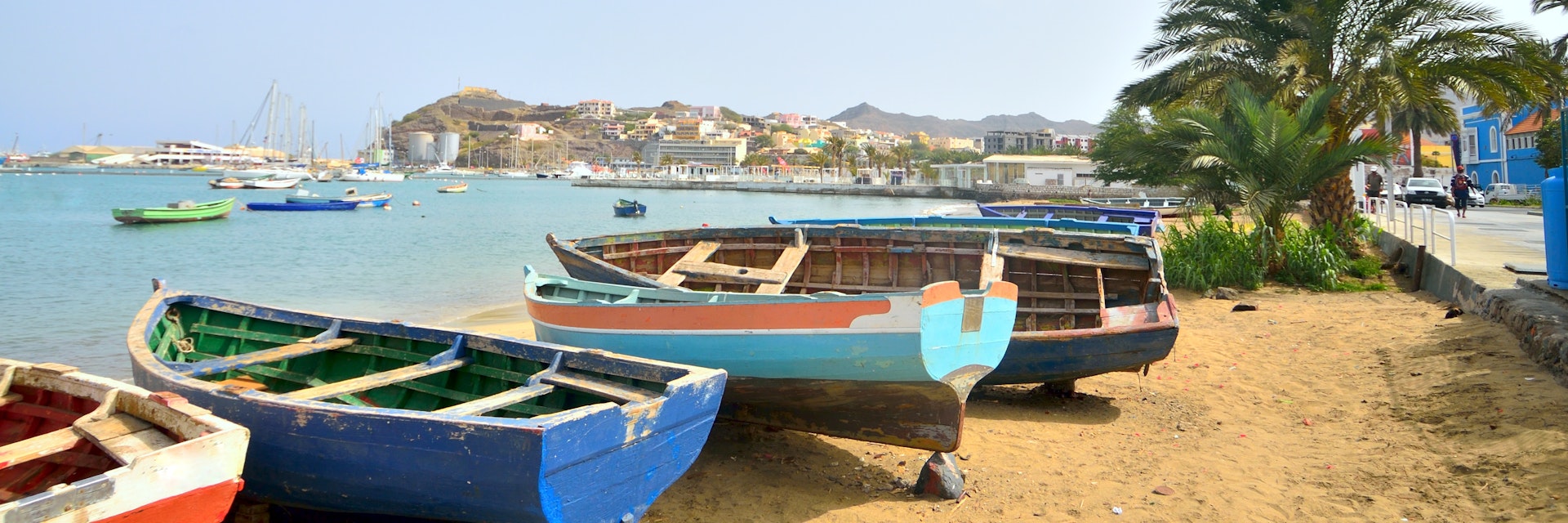 A collection of fishing boats beached on Mabota Beach in Mindelo with more luxurious sailboats in the background