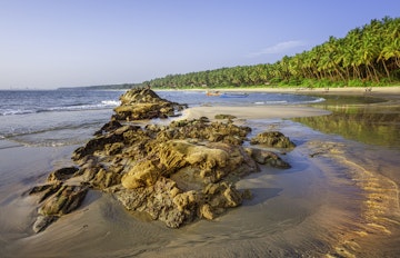 Kannur, December 10, 2011: Sunbathers and fishermen with boats on Cherai beach showing rocks formations in the foreground and coconut palms as backdrop at sunset along Malabar coastline, Kannur, Kerala, south India.