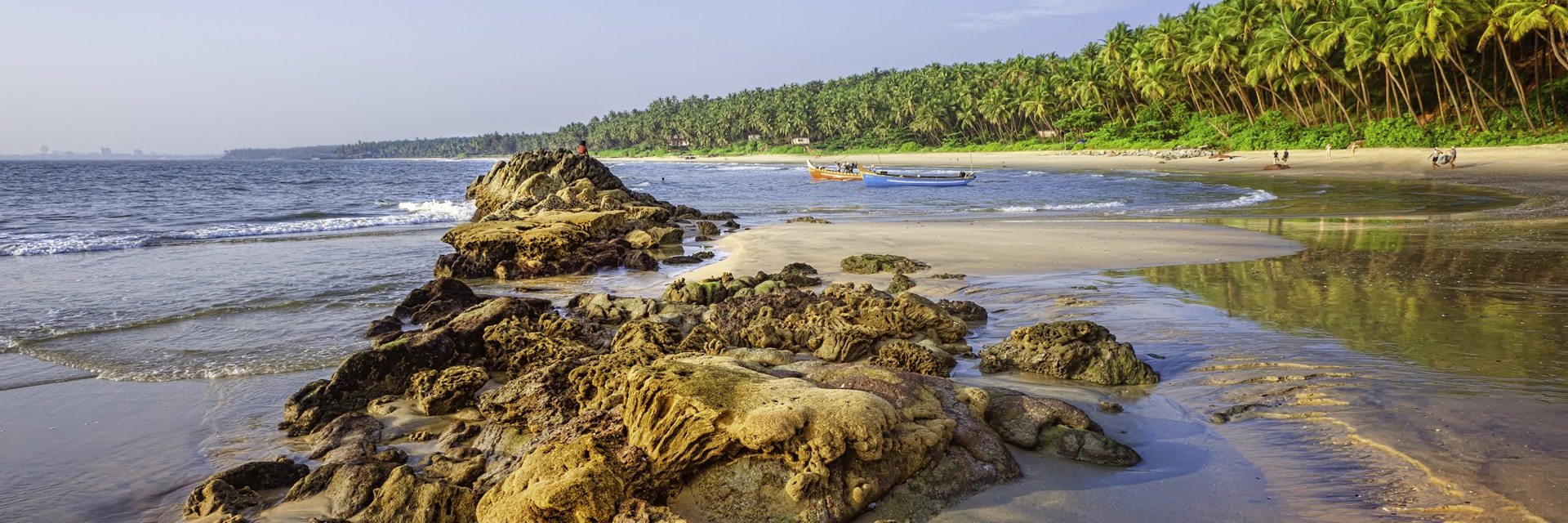 Kannur, December 10, 2011: Sunbathers and fishermen with boats on Cherai beach showing rocks formations in the foreground and coconut palms as backdrop at sunset along Malabar coastline, Kannur, Kerala, south India.