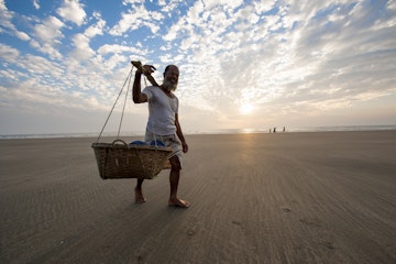 "Cox's Bazar, Bangladesh - February 10, 2013: A man is carrying seafood in barrel on shoulder walking on the beach of Cox's Bazar, Bangladesh."