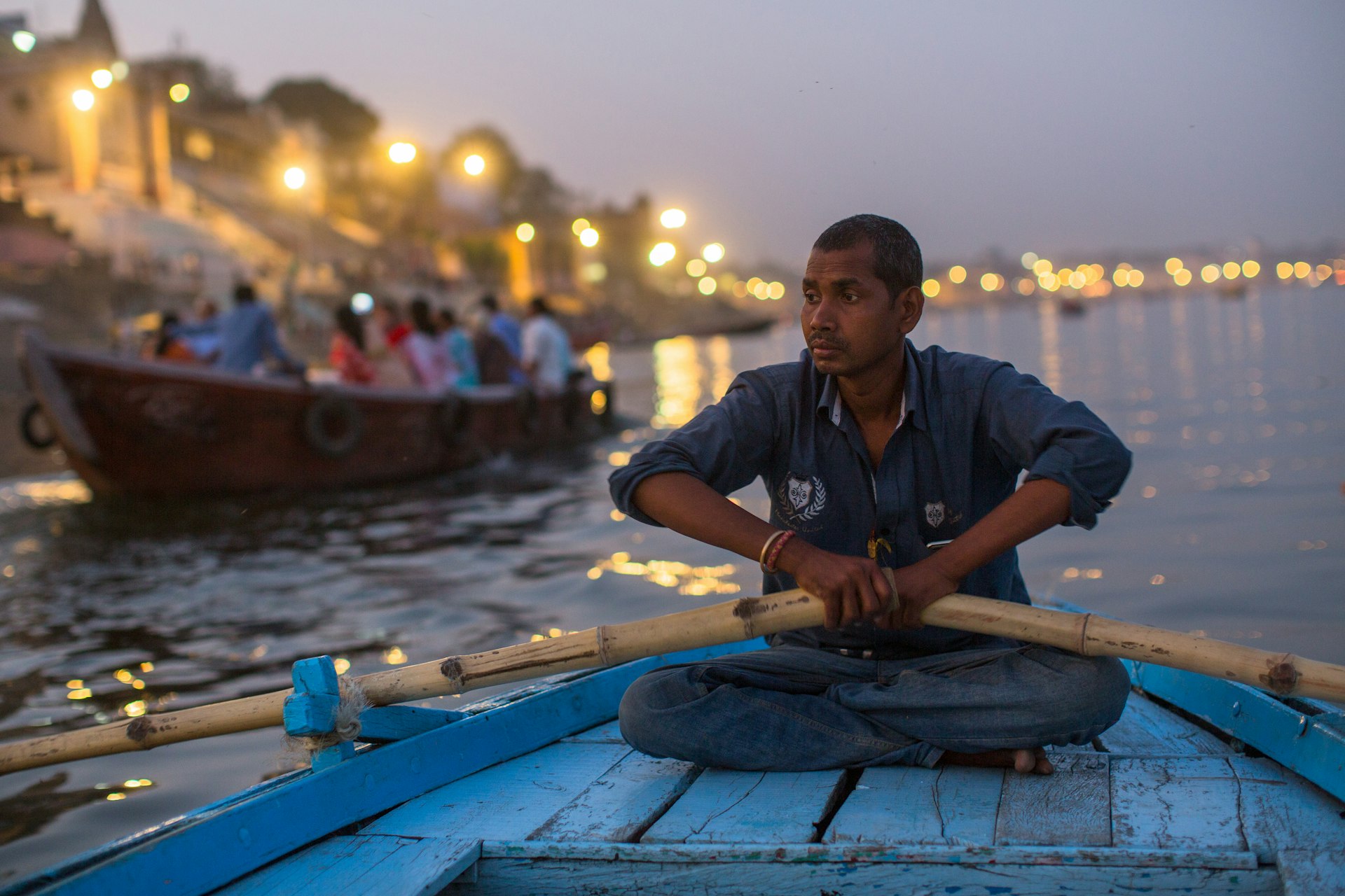 Close-up of a boatman holding oars on the Ganga River at night, Varanasi, India