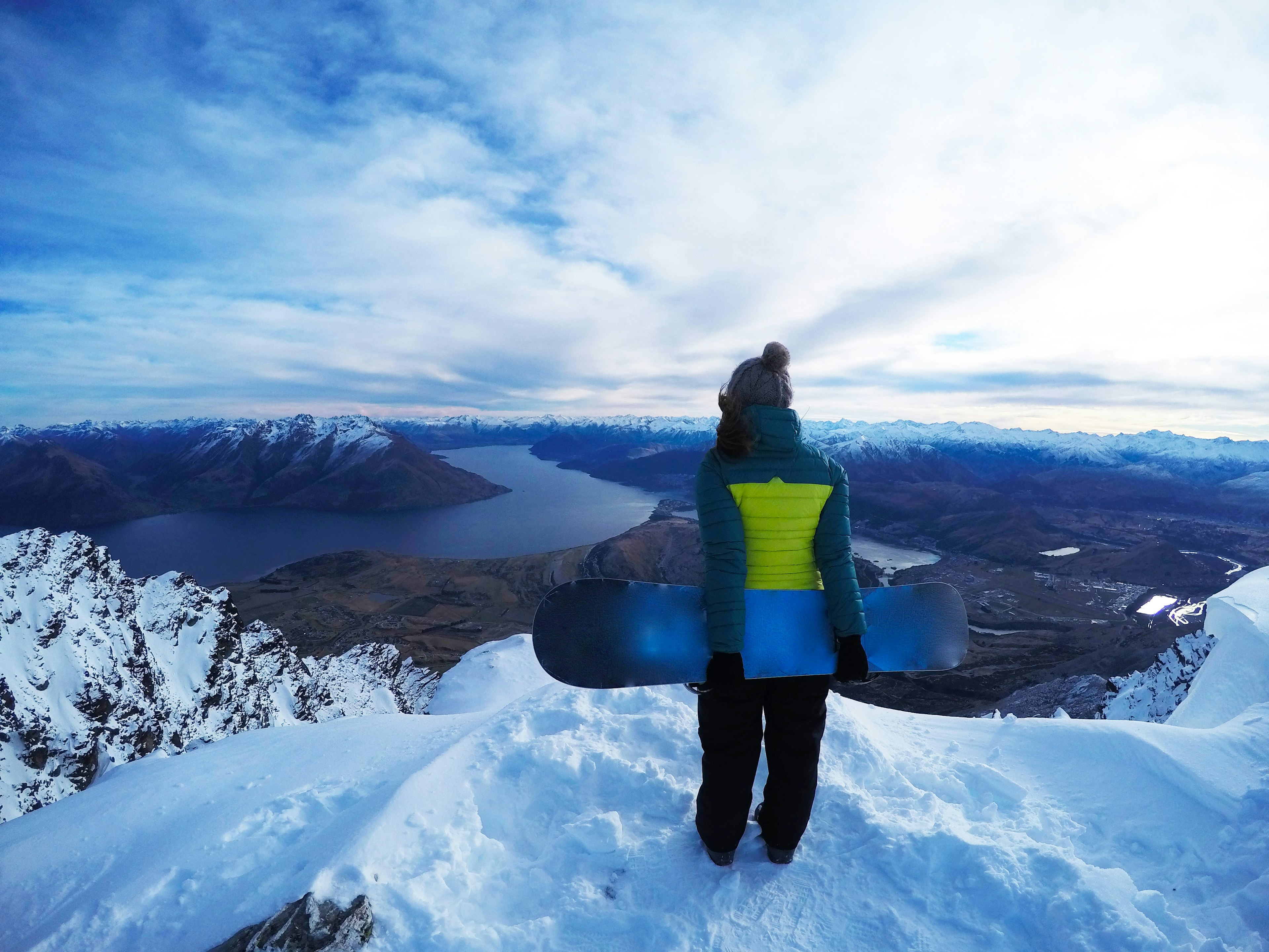 A woman holding a snowboard at the top of a snowy mountain at the Remarkables Ski Area