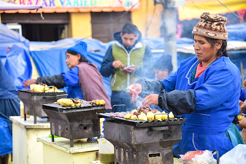 A woman cooks meat and potatoes at a street food stall in Potosi