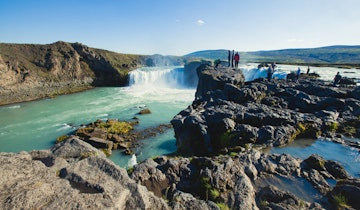 Visitors stand on rocks at the Goðafoss waterfall.