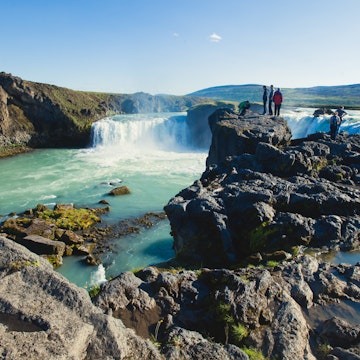 Visitors stand on rocks at the Goðafoss waterfall.