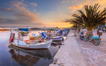 Fishing harbor scene in Greece with boats, palm trees and scooters at sunrise on a beautiful tranquil summer day