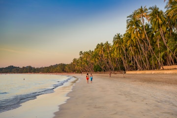 Couple walking on the palm-lined Ngapali beach during sunset.