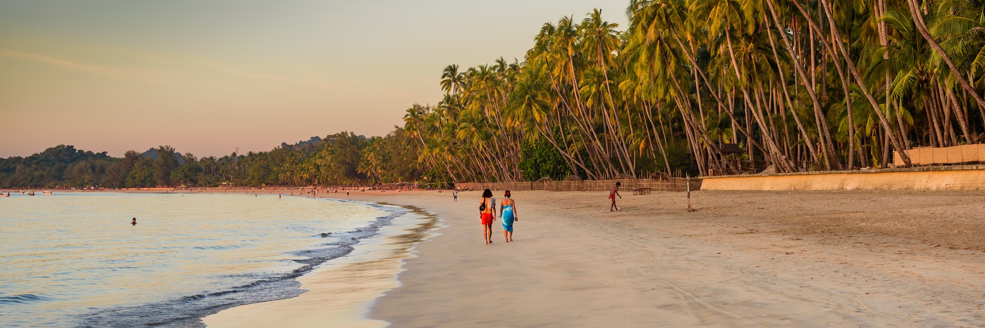 Couple walking on the palm-lined Ngapali beach during sunset.