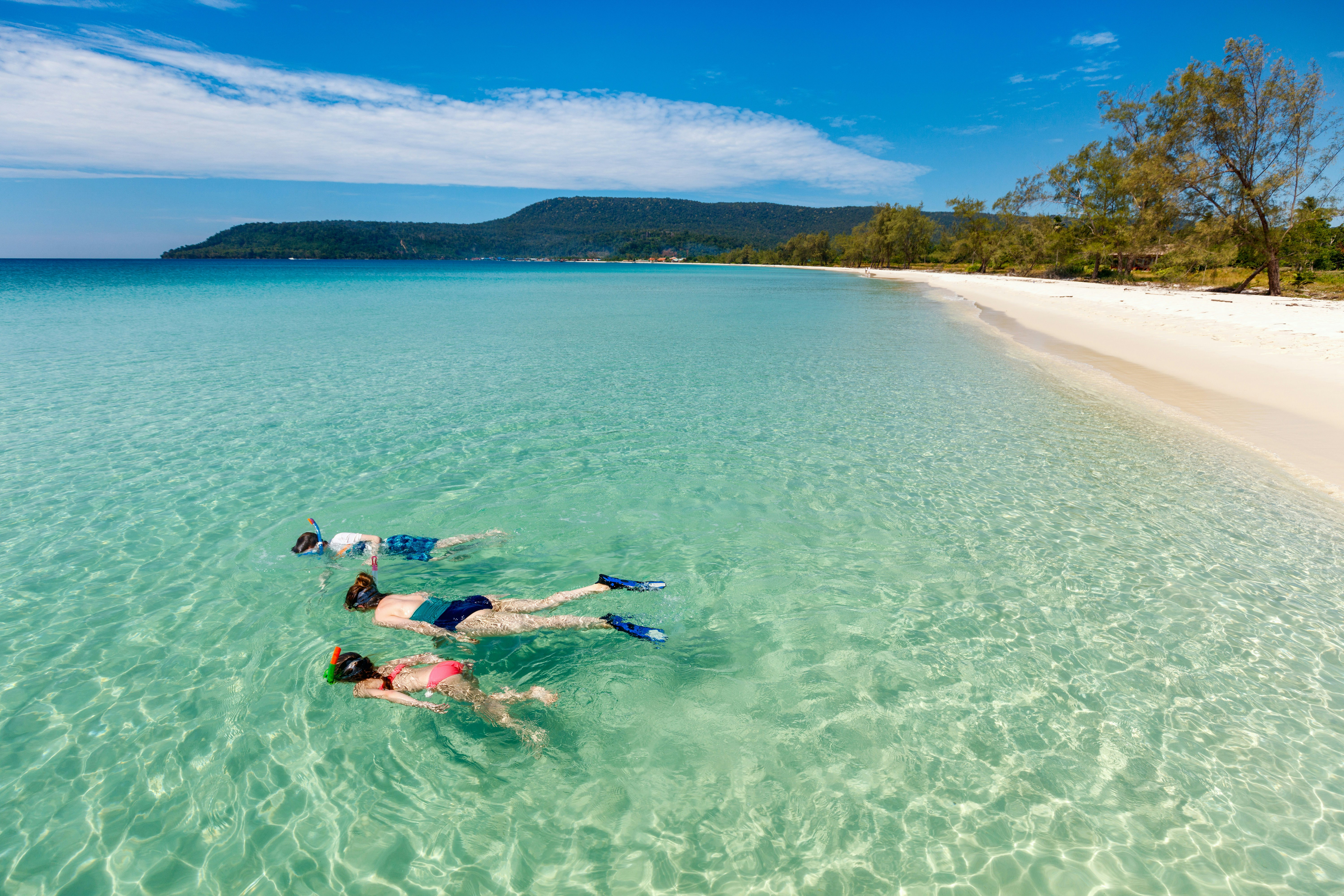 A mother and kids snorkeling in clear tropical water on an empty beach on Koh Rong, Cambodia