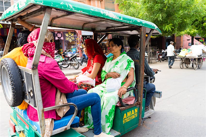 An auto-rickshaw (tuk tuk) driver carrying four passengers on a street in Jaipur