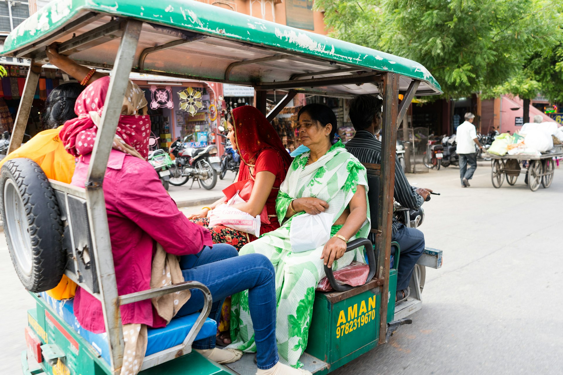An auto-rickshaw (tuk tuk) driver carrying four passengers on a street in Jaipur