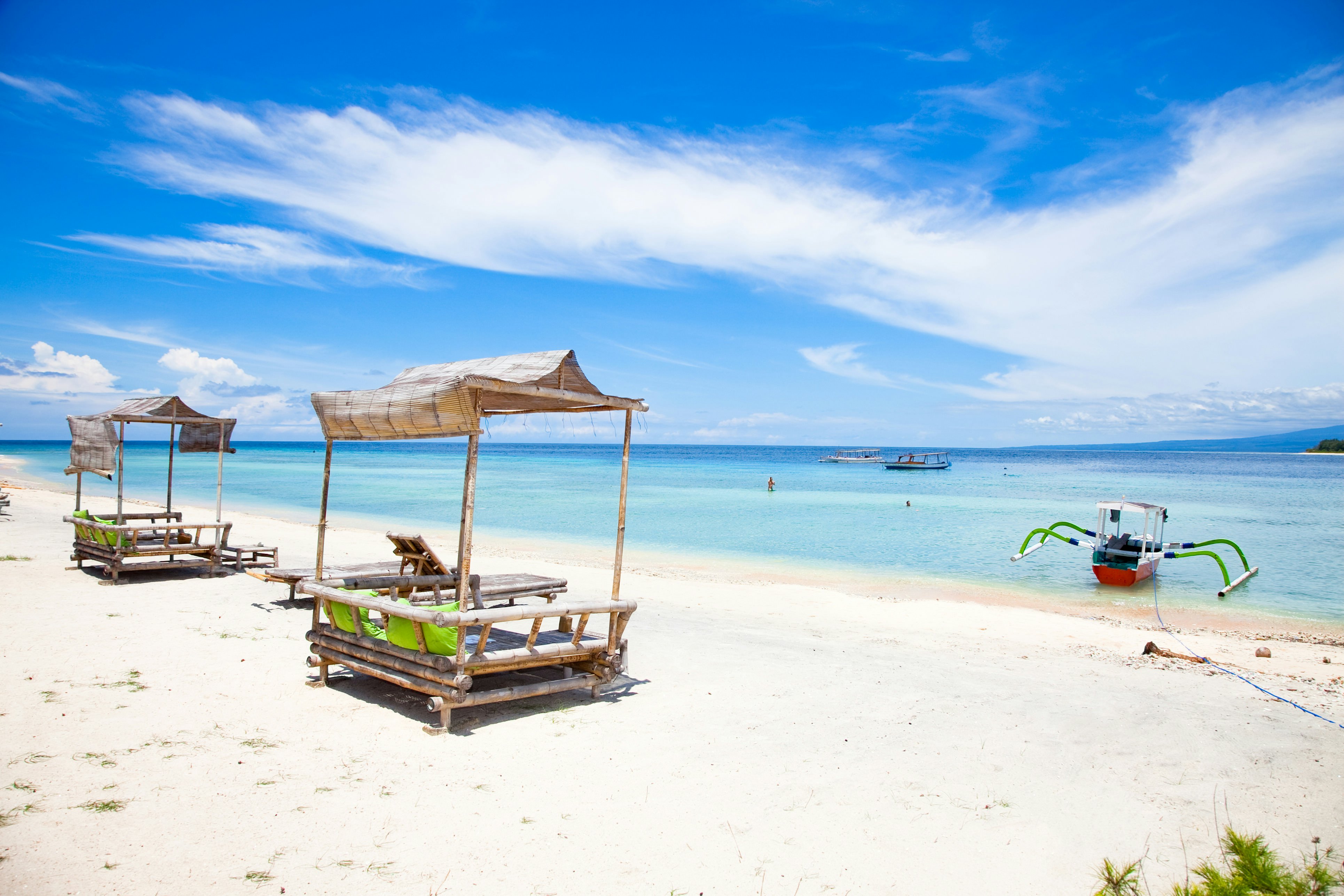 Two palm-thatched beach shelters on a white-sand beach next to turquoise ocean