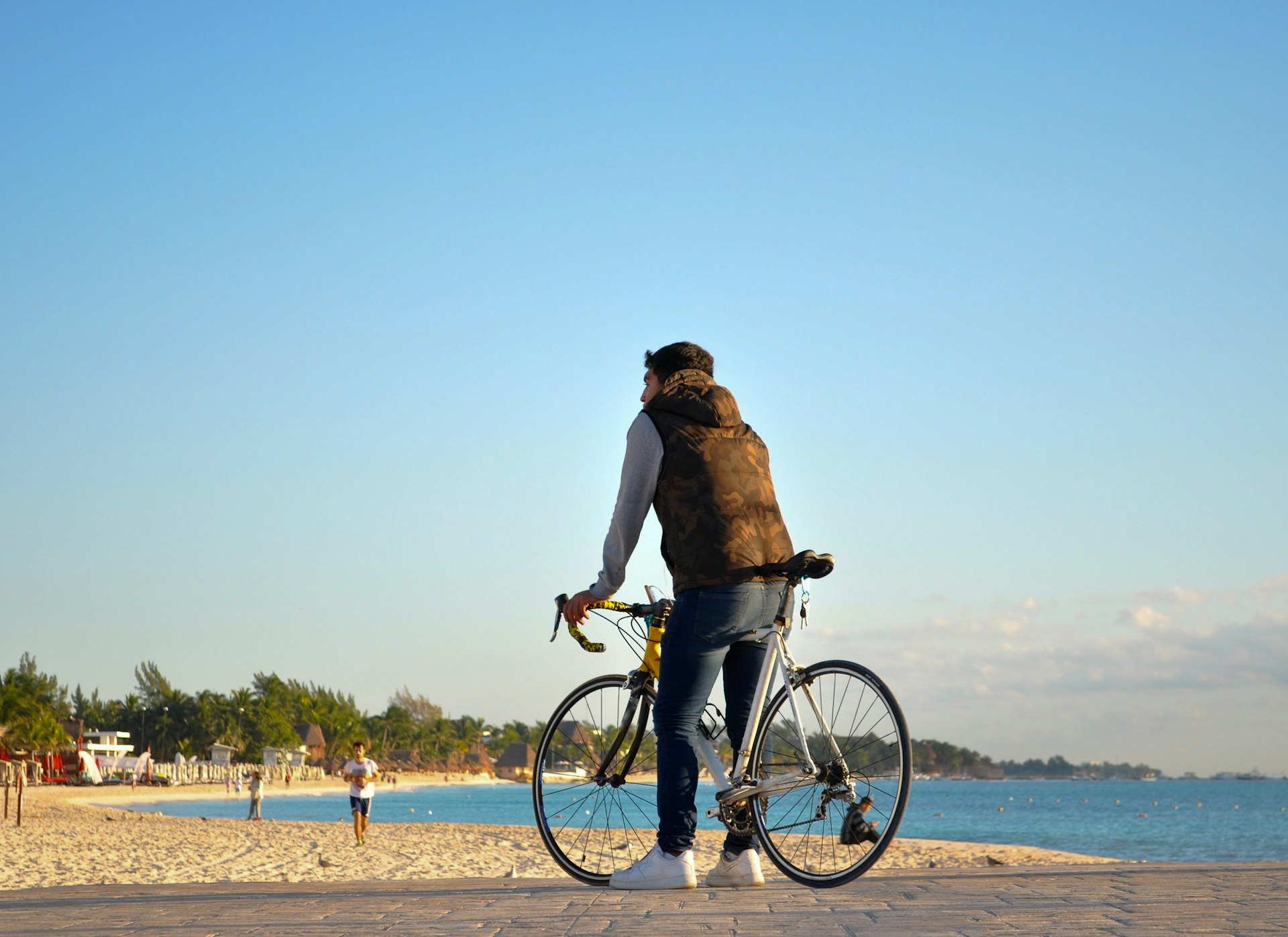 Young male standing on the beach with his bike with ocean and sky in the background, Playa del Carmen