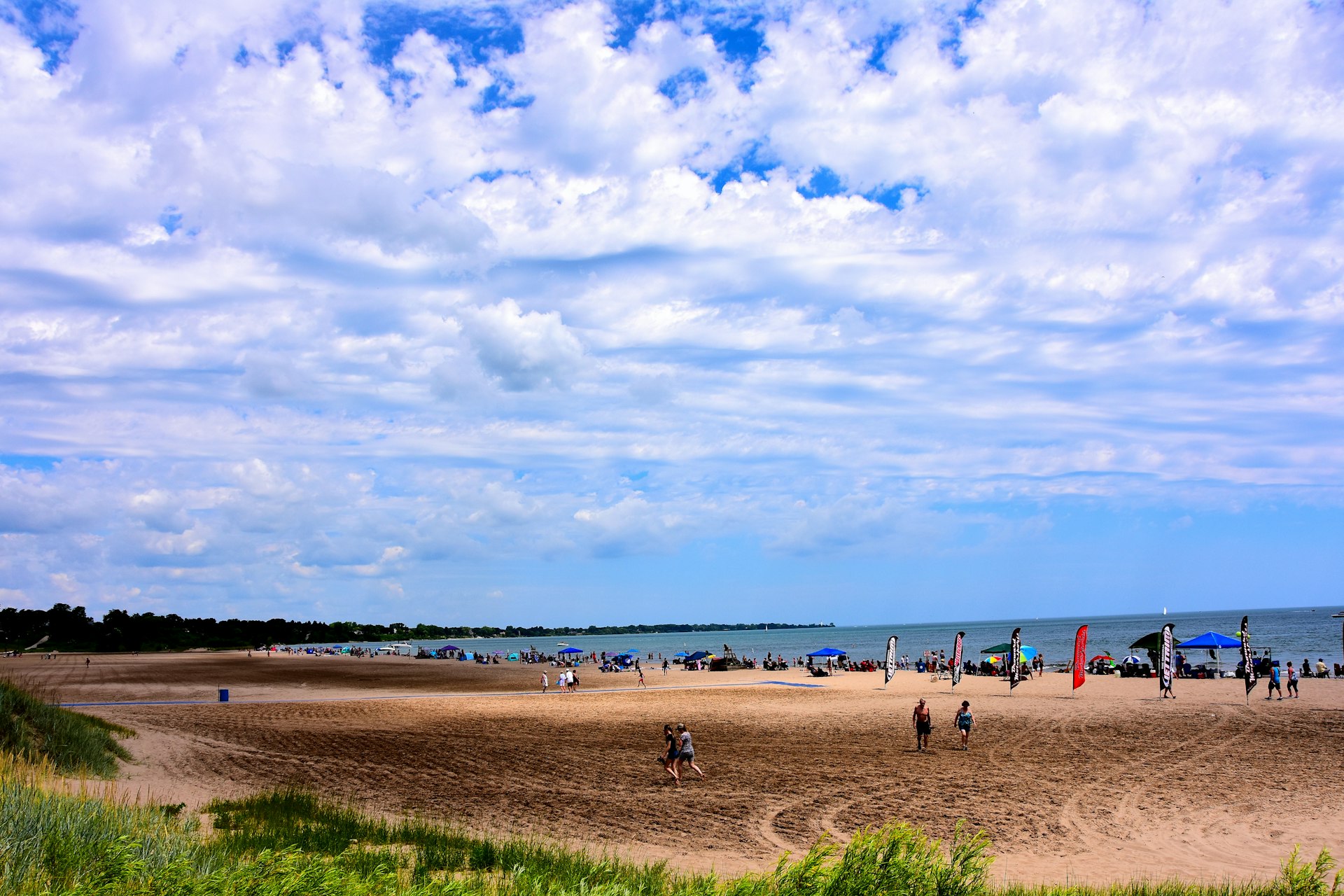 Many people enjoying the beach activities at North Beach on a beautiful summer day with clouded skies above the cool waters of Lake Michigan