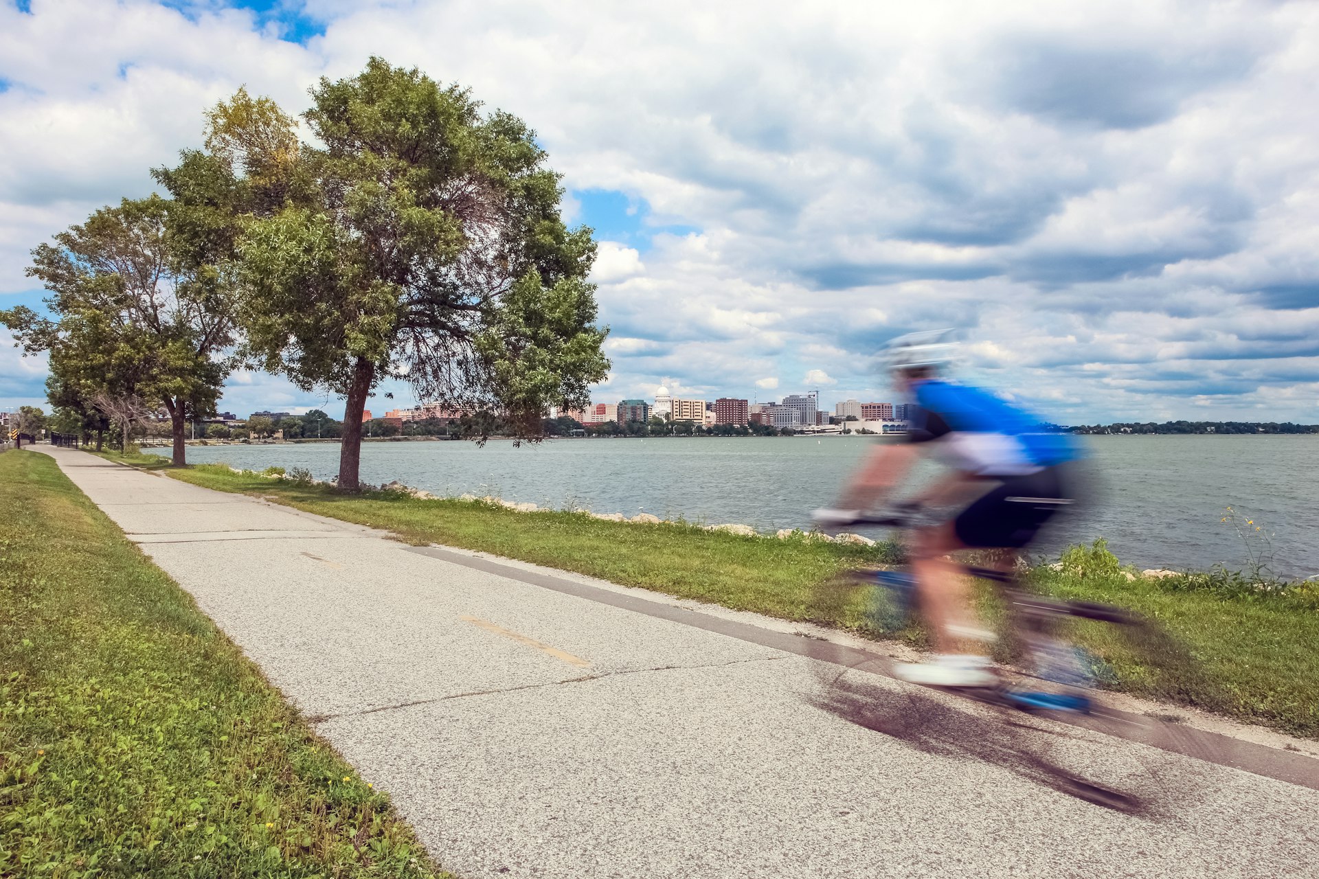 Motion blur of a person riding a bicycle on a lakeside bike path in Madison, Wisconsin with green trees and grass