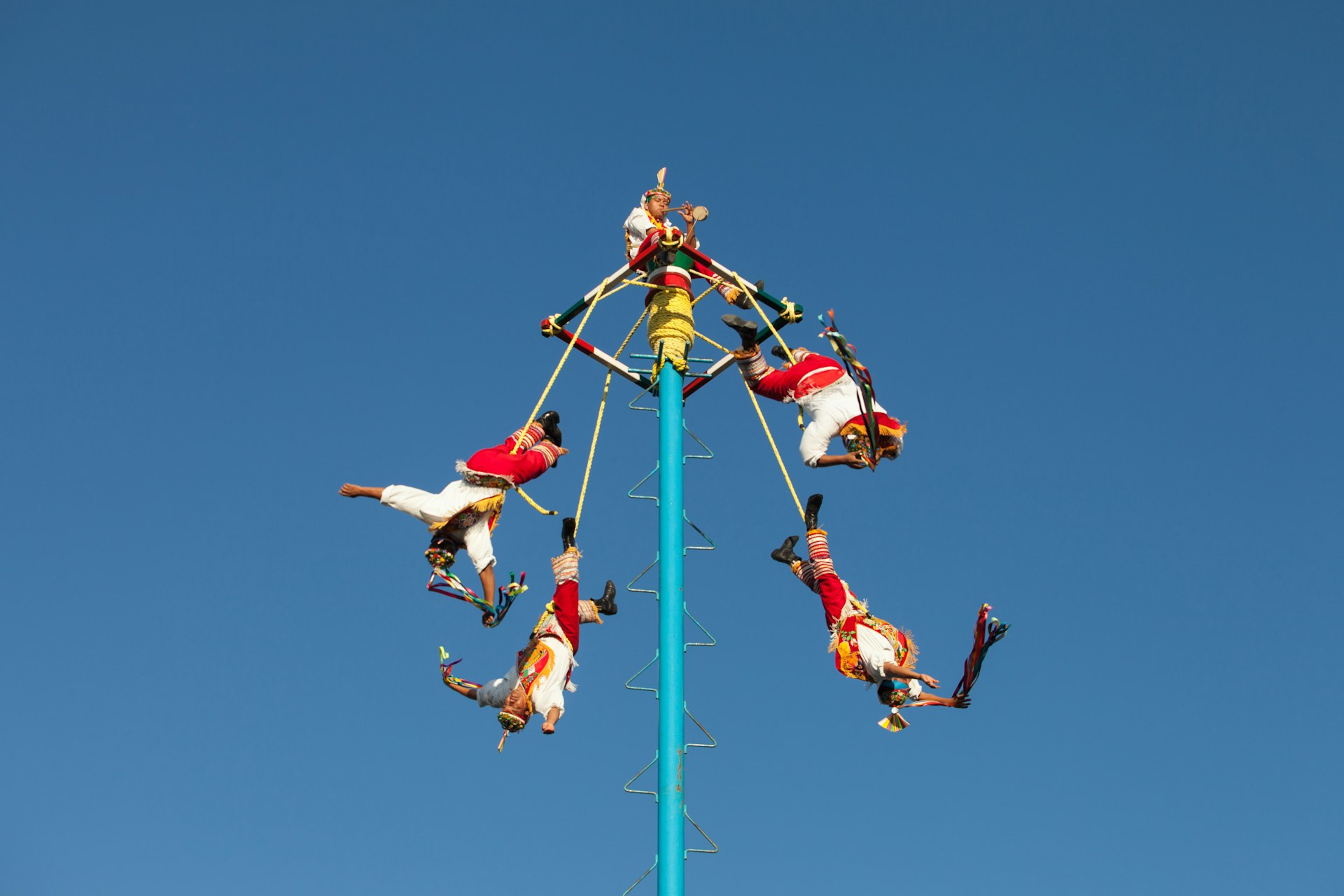Five flying acrobats (or “voladores”) enact their ritual, flying off a pole in traditional costumes suspended by their feet