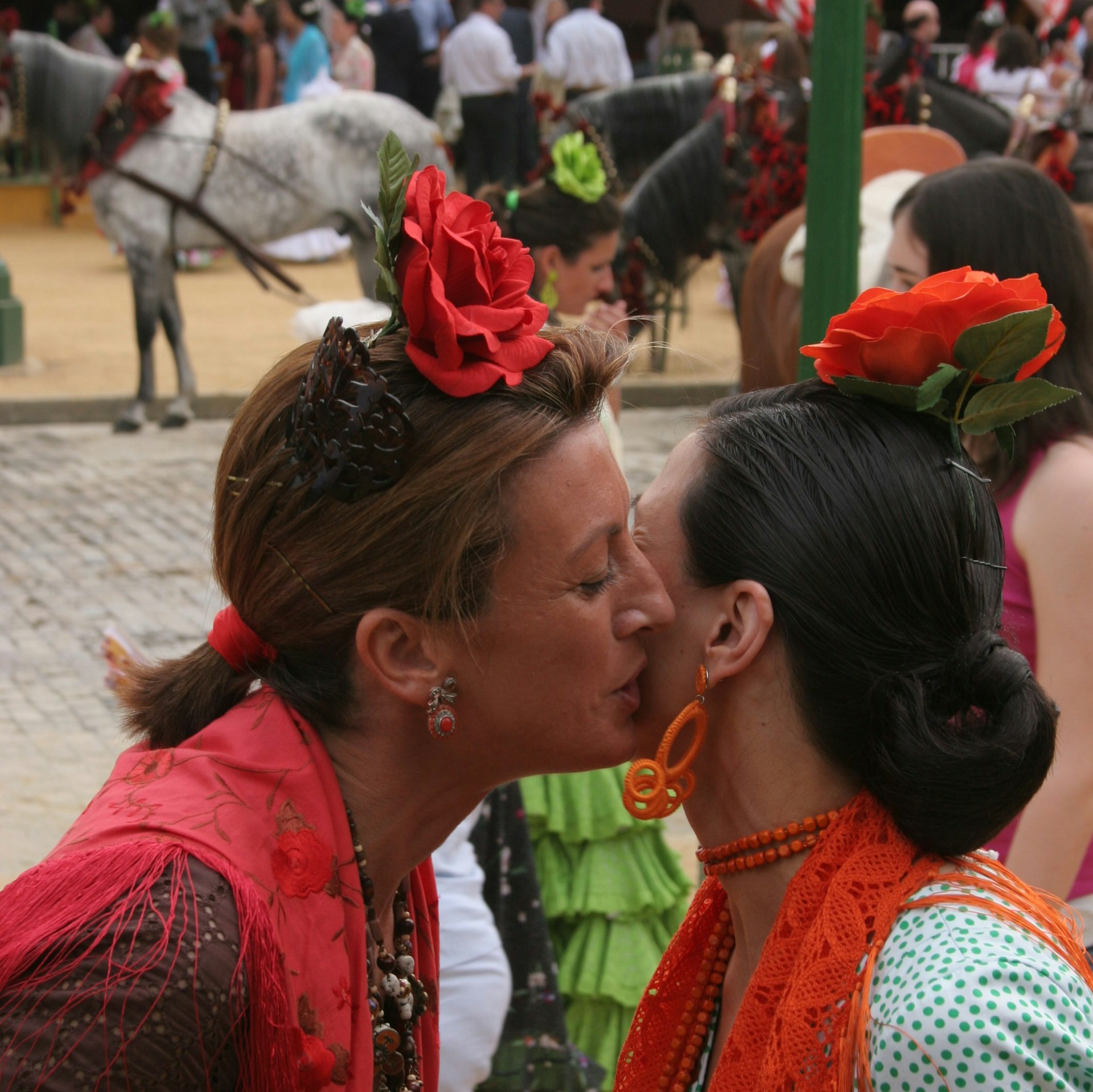 Two women in red millinery kissing at a street festival in Seville, Spain