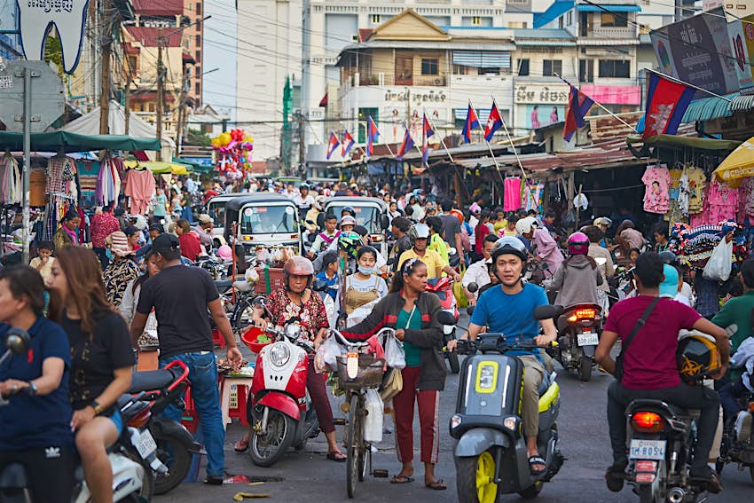 A crowded shopping street filled with scooter drivers and tuk-tuks in Phnom Penh, Cambodia
