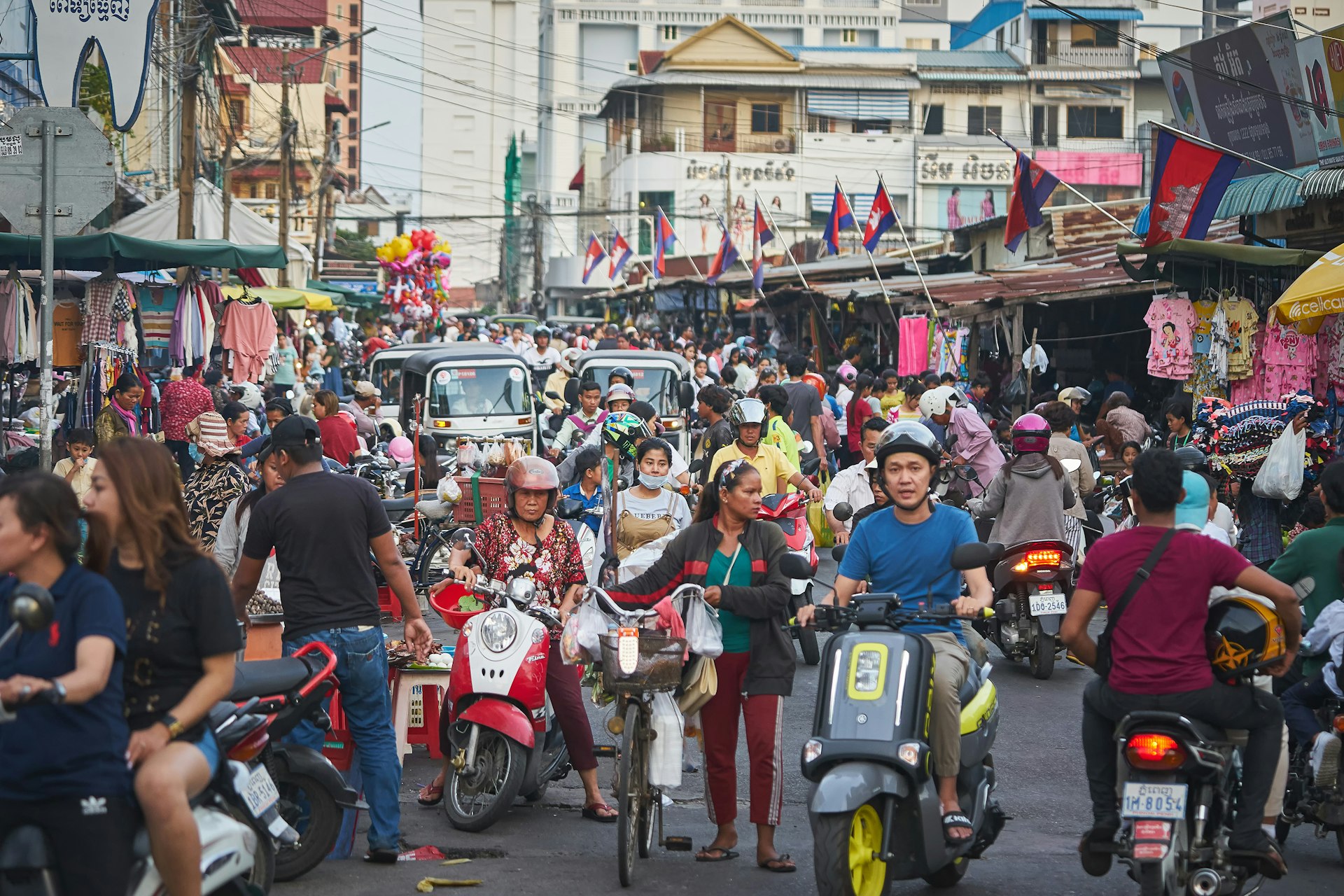 A crowded shopping street filled with scooter drivers and tuk-tuks in Phnom Penh, Cambodia