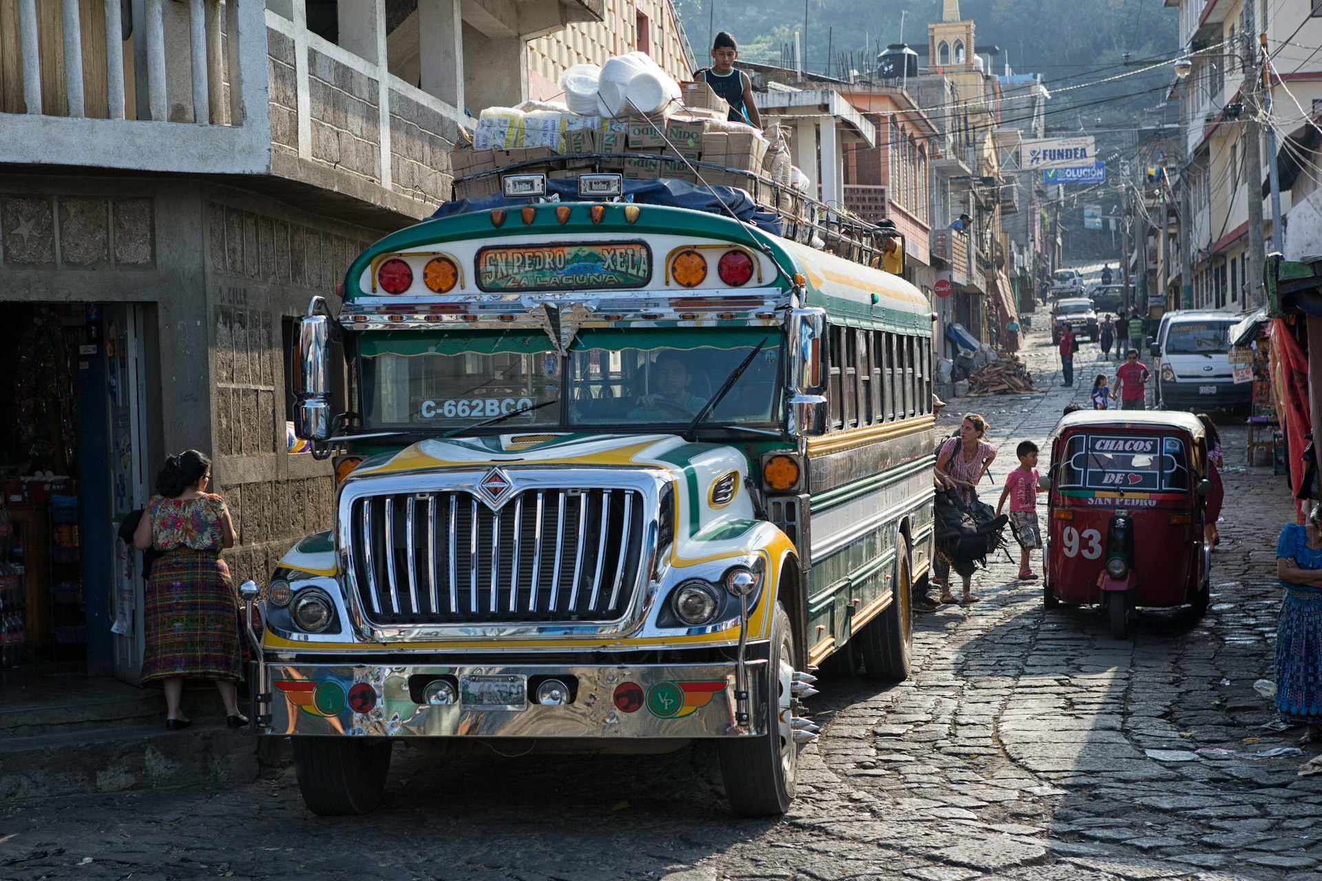 A colorful “chicken bus” (a repainted, purposed school bus) transports riders through the narrow cobblestone streets of San Pedro la Laguna, Guatemala