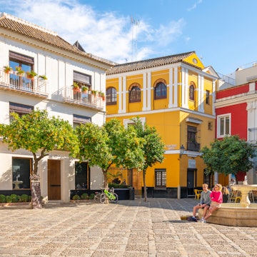 Seville, Spain - November 26 2021: Tourists and Spaniards enjoy a sunny autumn day in the Barrio Santa Cruz Plaza de la Alianza next to the Alcazar, a small square with public fountain and cafes