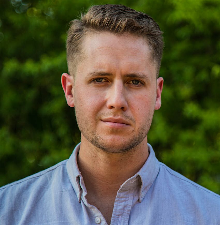 Alexander Howard A man stands in front of a green background looking at the camera in a portrait.