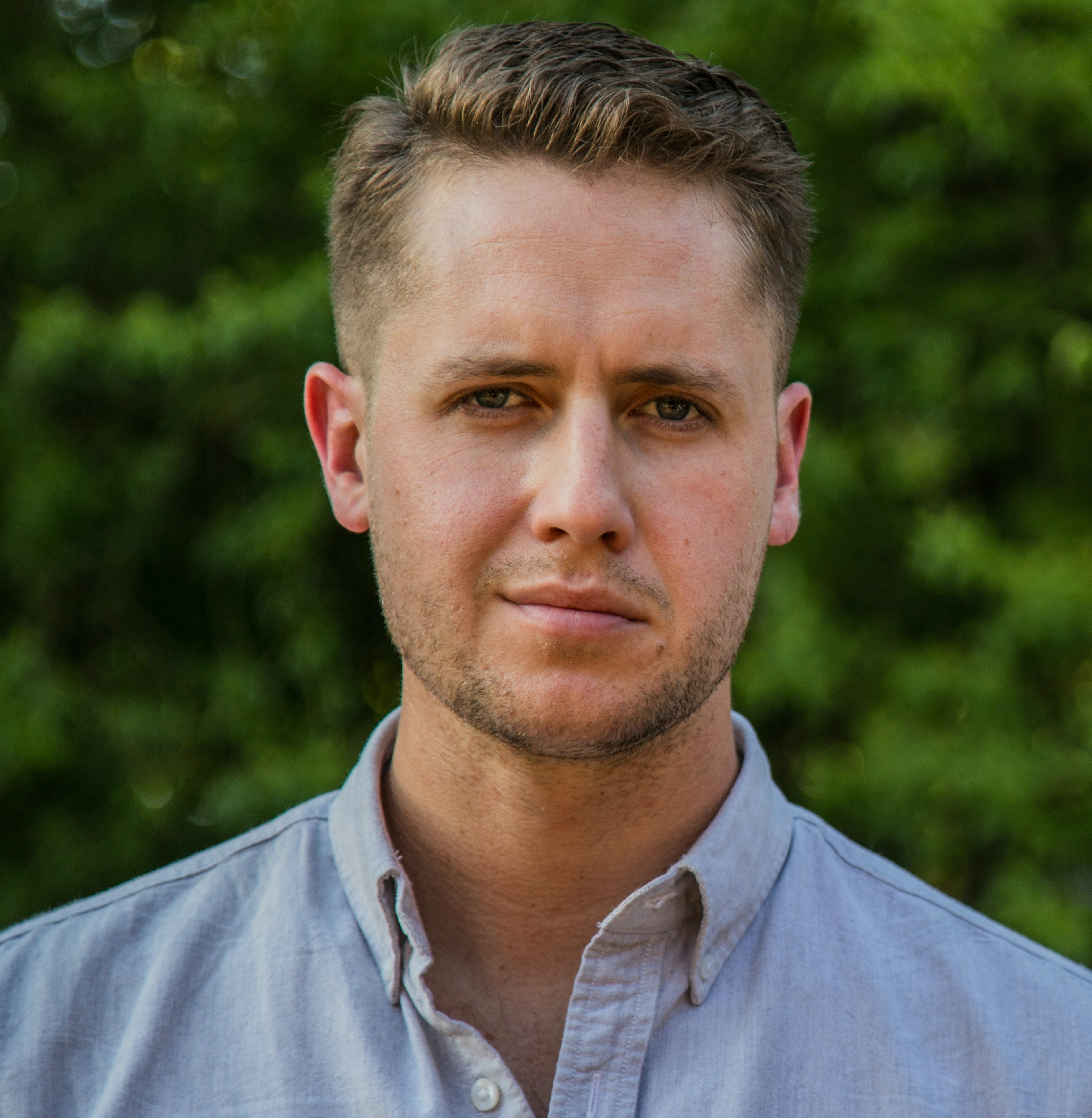 A man stands in front of a green background looking at the camera in a portrait.