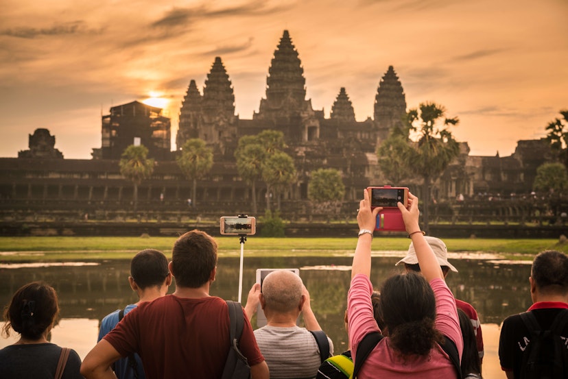 A group of people facing Angkor Wat and taking pictures as the sun comes up